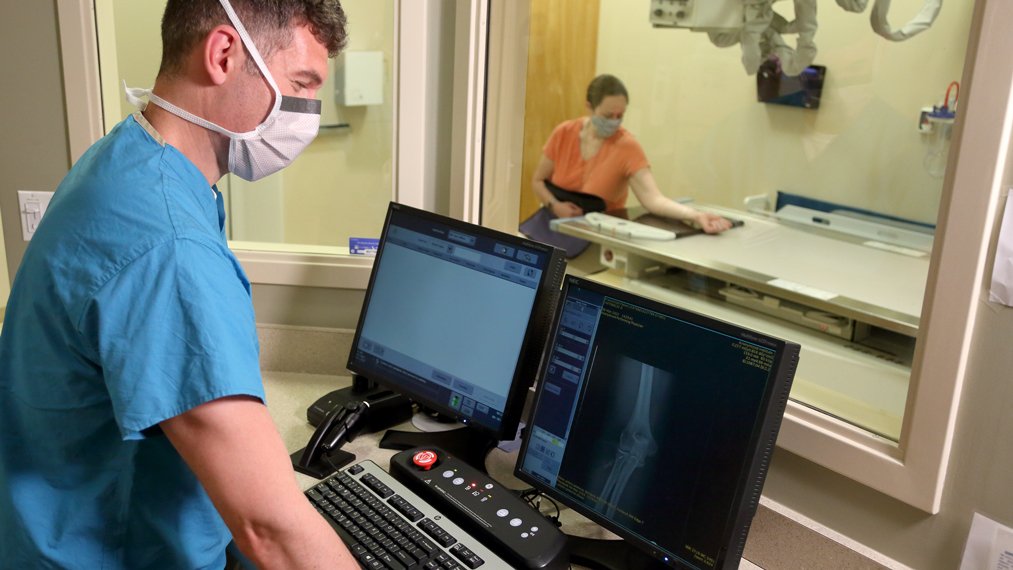 male x-ray tech looking at computer while female patient is being scanned