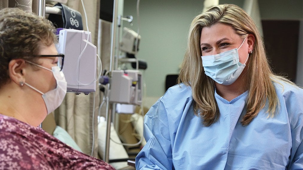 Masked female nurse provides chemo to female patient